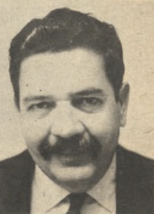 A black and white portrait of a man with a thick mustache and dark, neatly combed hair, and wearing a dark suit with a white shirt.