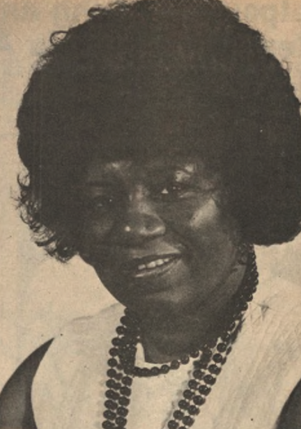 A portrait of a Black woman with a medium-length afro hairstyle, wearing a sleeveless top and a beaded necklace. 