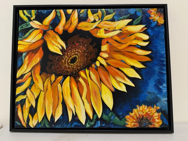 A large vivid painting of sunflowers in yellow and orange against a deep blue background, displayed in a black frame