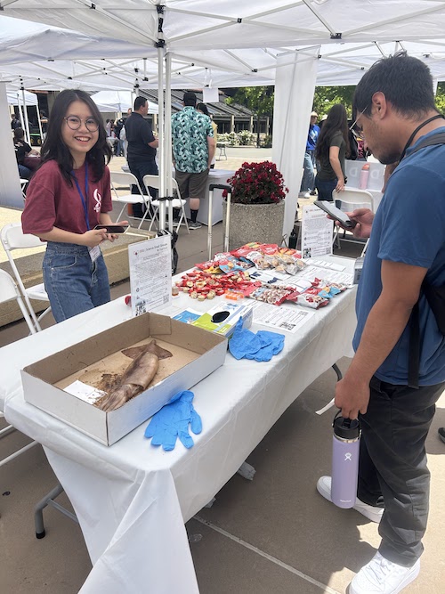 young woman speaking to students at information table