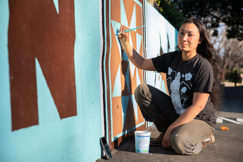 Meesha Goldberg: woman in blue shirt painting a mural