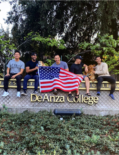 young men with flag sitting on De Anza entrance sign